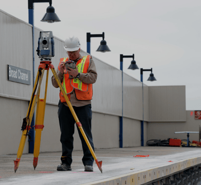 a man in a hard hat and safety vest using a tripod