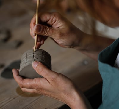 femme gravant des motifs à la main avec un outil en bois sur l'argile dans l'atelier de poterie