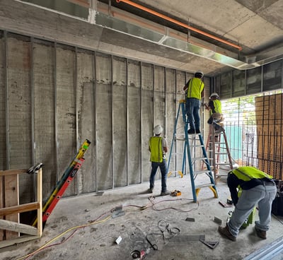 Construction workers installing metal stud framing in a commercial building under construction, with exposed concrete ceiling