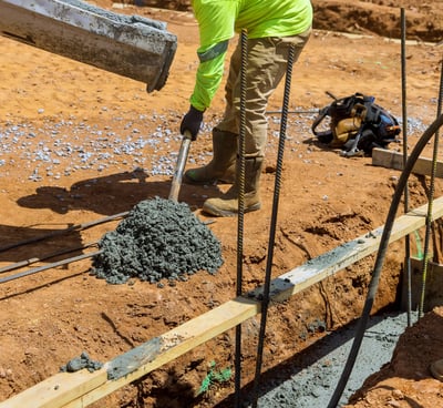 a man in a yellow jacket is pouring concrete into a concrete slab