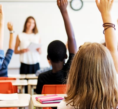 An image of a classroom with a teacher and students learning and raising their hands with curiosity