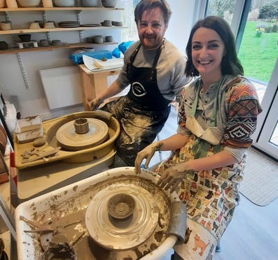 a man and woman are smiling and having fun in the pottery on the 2hr throwing workshop