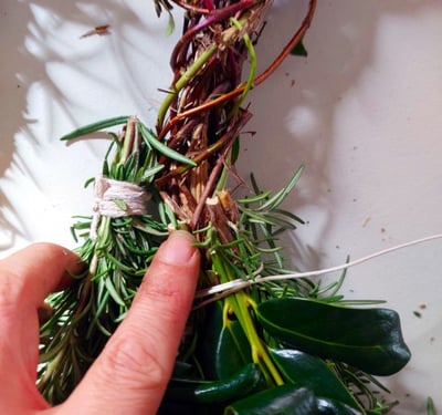 honeysuckle vine wreath and finger pointing to place rosemary bundle after cut ends of last bundle