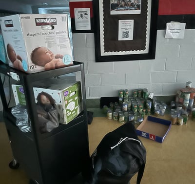 A dark middle school hall food pantry with cans of food and baby supplies during Hurricane Helene