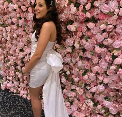 Bride to be in a white dress standing infront ouf our pink rose flower wall