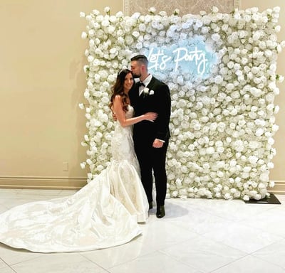 Newlyweds taking a photo in front of the white rose flower wall during their wedding