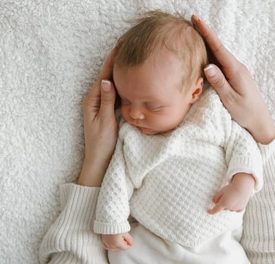 a newborn baby photoshoot. The baby is sleeping on a blanket. mum holding the baby in her hands