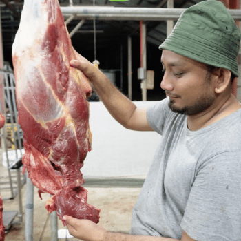 a man in a green hat and a large piece of meat on a table