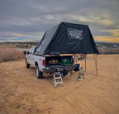 A truck with a fold-out overland tent on it's bed beside a lake