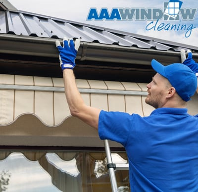 A man in blue cleaning gutters with gloves on