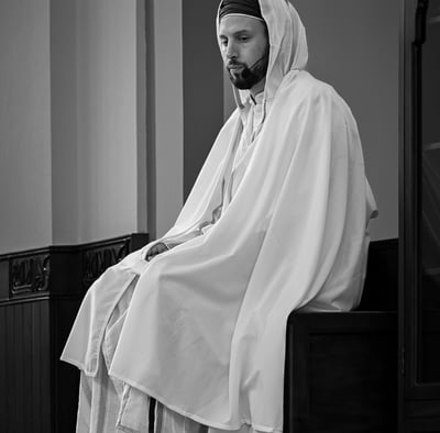 Imam of Imam Malik Mosque in a robe is sitting on a bench