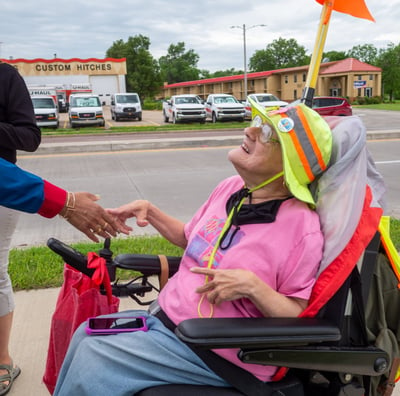 Photo of Dawn Zuterberg sitting in her electronic scooter, shaking someone's hand