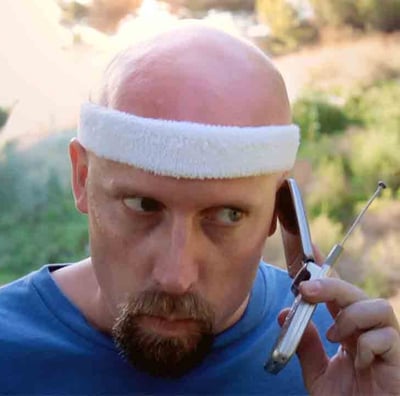 A man in workout attire listens to a call on his outdated cell phone