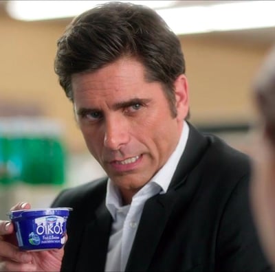 John Stamos holds an Oikos while talking to a cashier