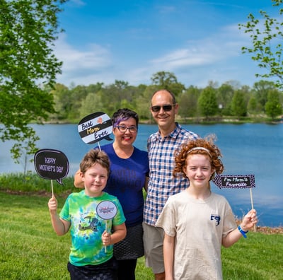 Two parents and two children posing in front of a lake holding sign props