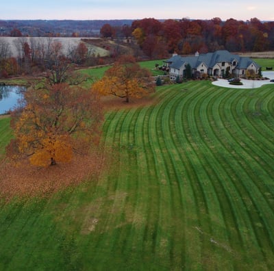 A large house with a spacious yard, a pond, and vibrant autumn-colored trees surrounding the propert