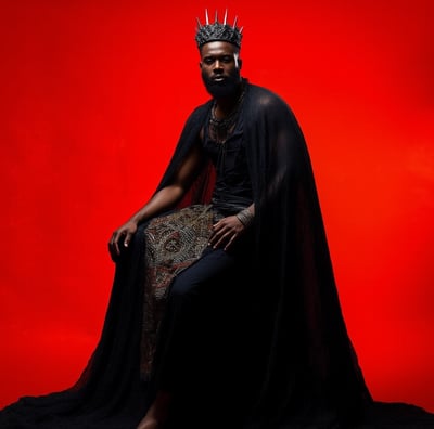 a black man with a crown and capelet dress