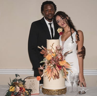 Bride & Groom posing for a photo by their three tiered cake before cutting