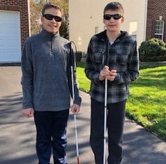 Two boys holding white cane.