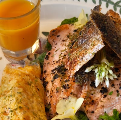 Rolled egg, salmon with crispy skin, wild garlic flower garnish, sea buckthorn juice