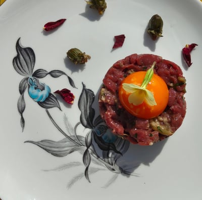 Venison tartar with an egg yolk, primrose garnish, dandelion capers and rose petals