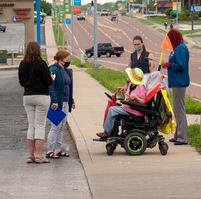 Group gathered on the sidewalk of a busy street