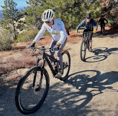 two people riding bikes on a dirt road