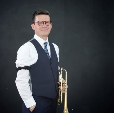 George Chase wearing a vest, tie and arm garters, holding a cornet.