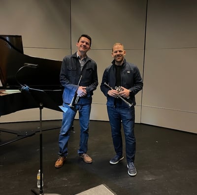 George Chase and Caleb Hudson smile, holding piccolo trumpets, during a rehearsal break.