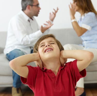 a young boy is holding his ears as a man is sitting on a couch with a woman holding her hands up. 