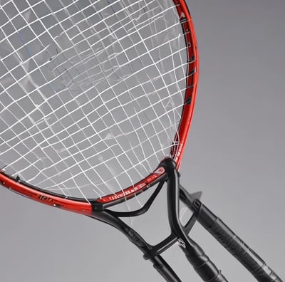 A worn badminton racket with a red and white frame is resting on a moss-covered concrete step. The racket's strings are slightly sagging, indicating it is old or well-used. The surrounding surface has patches of green and gray, with some small stones and worn areas visible.