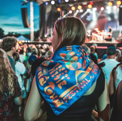 A vibrant crowd at an outdoor music festival at night, focusing on a young woman wearing a polyester scarf with printed the l