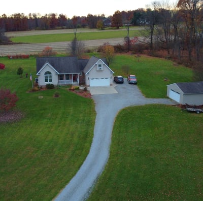 A country house with a separate garage and a long driveway, surrounded by open land.