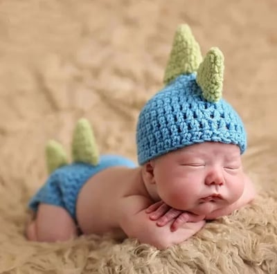 a baby boy wearing a blue crochet dinosaur hat and pants
