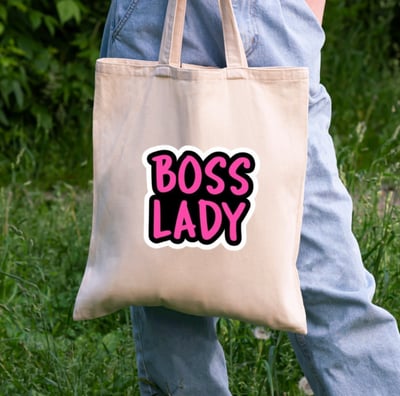 a person holding a tote bag and a written text on bag is "Boss lady".