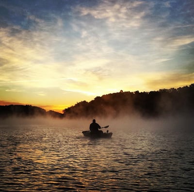 a man in a kayak on a lake at sunset