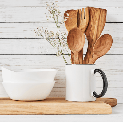 Wood spoons and laddles placed in a coffee cup with ceramic bowls besides.