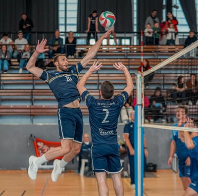 Joueur qui fait une passe à un autre joueur qui saute pour attaquer