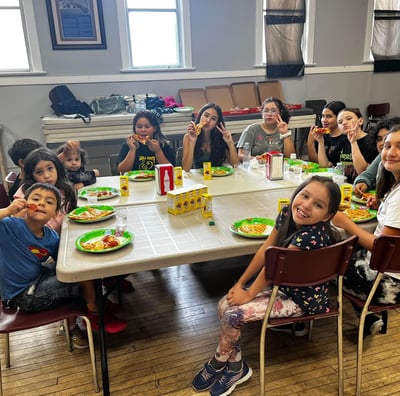 a group of children sitting at a table with plates of food
