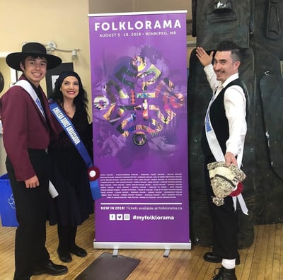 a man and woman standing next to a Folklorama banner
