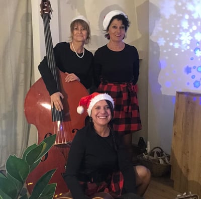 trois femmes en robe rouge et noire à carreaux avec des bonnets de Noël et une contrebassess