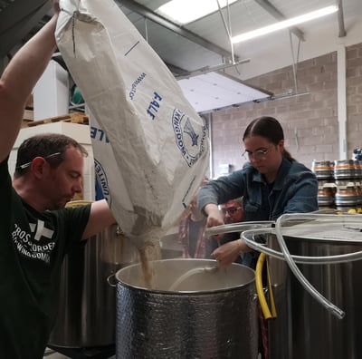 Brewer pouring malt into tank for a collaborative beer using pineapple weed