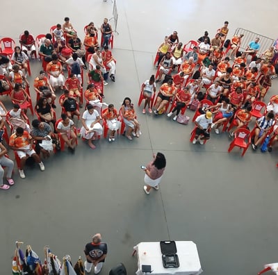 uma mulher ao centro e varias pessoas sentadas em cadeiras