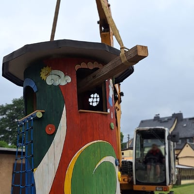 der bunte Spielturm aus Holz wird an Schleppen zum Standort gehoben