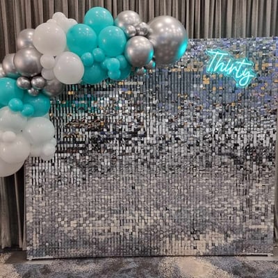 Silver shimmer wall with a glowing aqua Thirty neon and silver white and aqua balloon garland at Logan event.