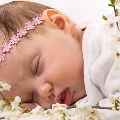 a baby lying on her front, wearing garland of flowers around her head