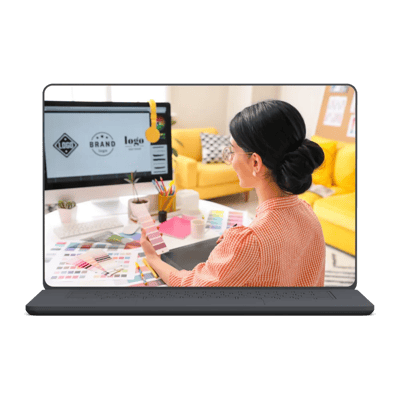 Woman in checked shirt reviewing color swatches while designing graphics on laptop in a cozy workspace.