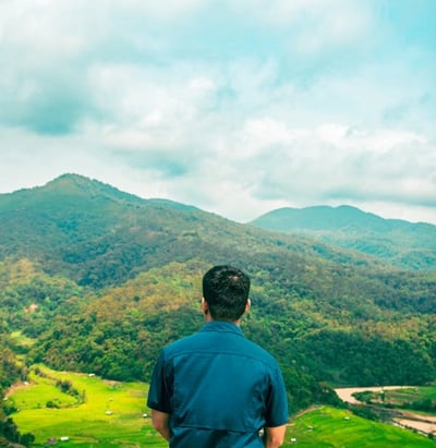 Homme de dos assis en montagne regardant une vallée et les sommets verdoyants