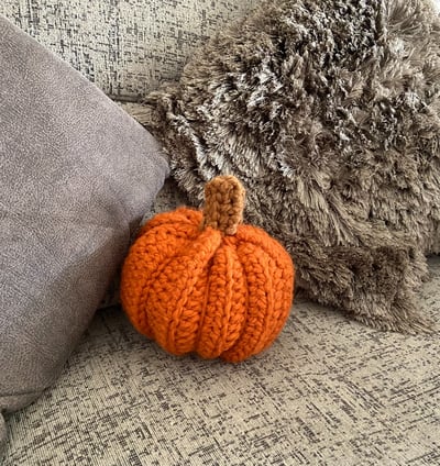 Handmade crochet pumpkin on a sofa with two cushions.