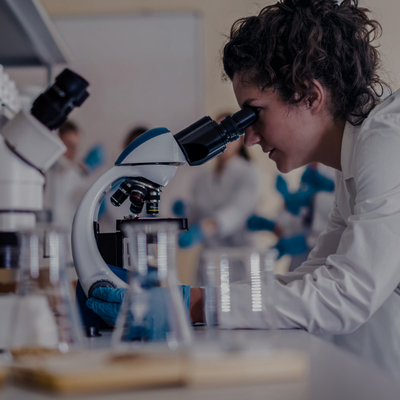 a woman in a lab coat is looking through a microscope